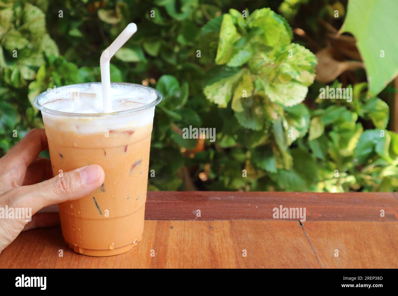 Main tenant une tasse de savoureux thé glacé thaïlandais sur la table de jardin Banque D'Images