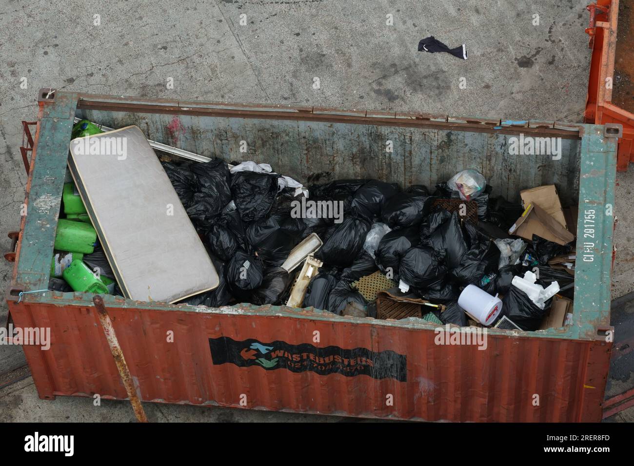 Conteneur orange à toit ouvert plein d'ordures dans des sacs en plastique noir situé sur la jetée dans le port du Cap. Banque D'Images