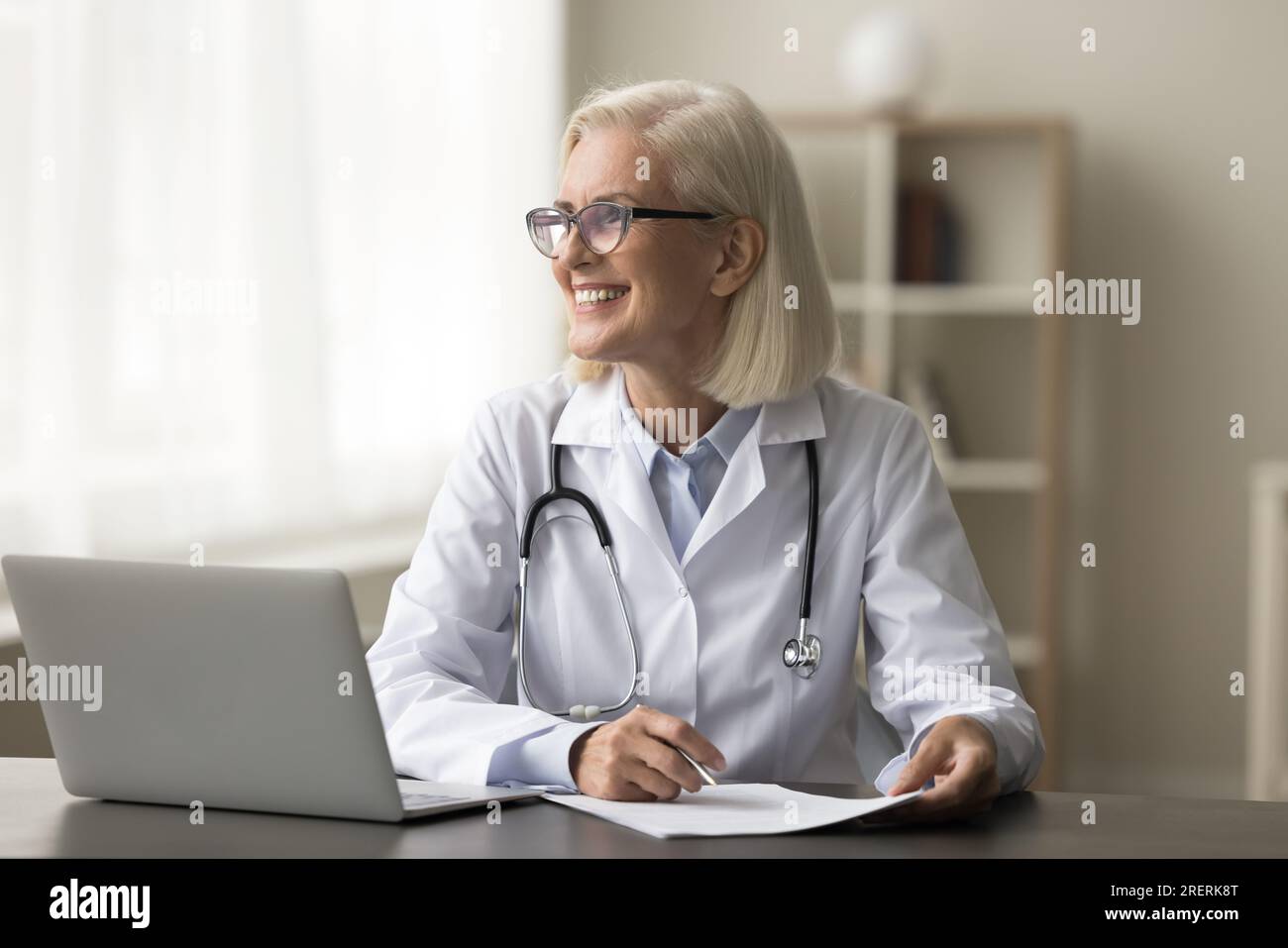 Femme médecin professionnelle mûre réfléchie heureuse assise sur le lieu de travail Banque D'Images
