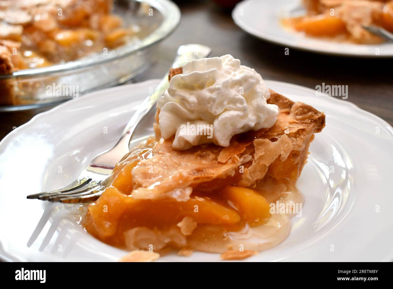 Une tranche de tarte aux pêches avec de la crème fouettée sur une assiette blanche Banque D'Images