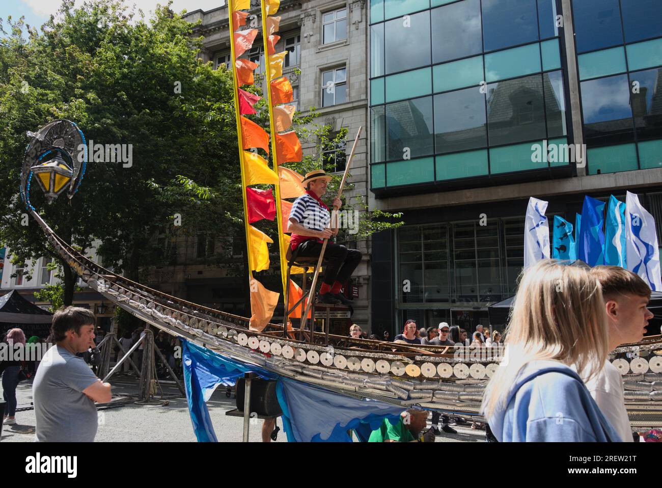 Manchester, Royaume-Uni, 29 juillet 2023. Un gondolier vénitien range sa gondole argentée le long de la rue, tandis que sous lui un homme pédale. Une jeune femme et un jeune homme passent devant. Manchester Day - On Holiday!, gratuit, amusant, familial, événements dans les rues du centre-ville Manchester, Royaume-Uni. Soutenu par Manchester City Council, Manchester Airport Group, Biffa, The Co-op, Manchester Evening News, Walk the Plank, Kingdom of Sweets, British Firefighter Challenge et Capri Beach Club. Crédit : Terry Waller/Alamy Live News Banque D'Images