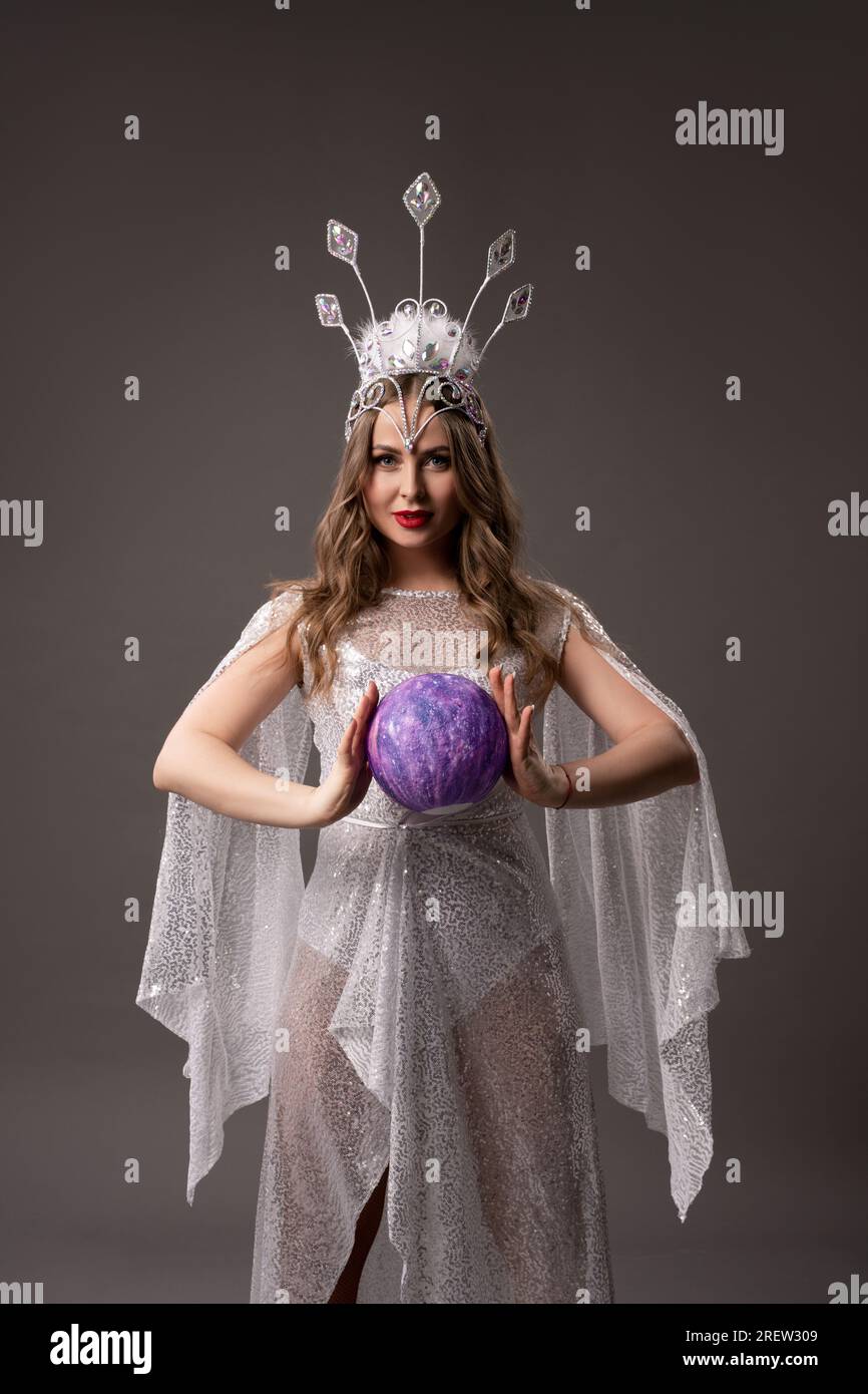 Douce fée en robe translucide blanche avec boule magique dans ses berges Banque D'Images