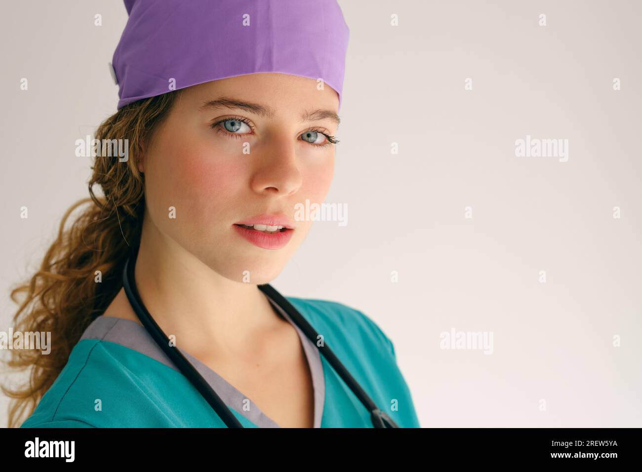 Contenu jeune femme avec les yeux verts en uniforme médical et chapeau violet regardant la caméra sur fond gris Banque D'Images
