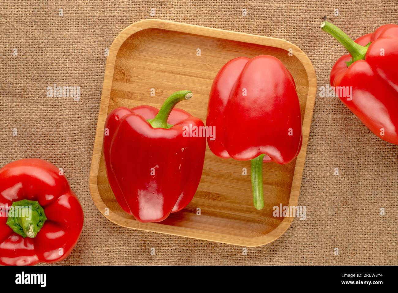 Quatre poivrons rouges doux avec plateau en bambou sur toile de jute, macro, vue de dessus. Banque D'Images