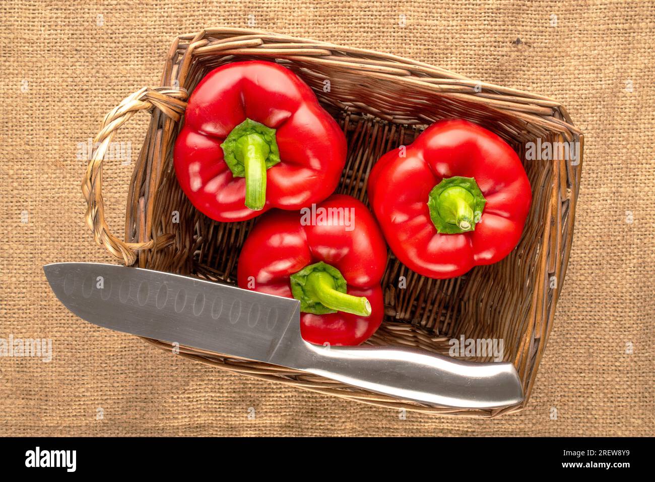 Trois poivrons rouges doux avec panier et couteau sur toile de jute, macro, vue de dessus. Banque D'Images
