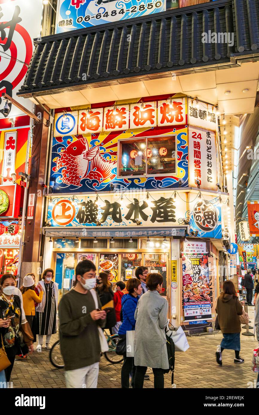 Scène animée des gens devant le populaire restaurant de fruits de mer illuminé Hamayaki BBQ dans la soirée, dans le quartier des divertissements, Dotonbori, Osaka. Banque D'Images