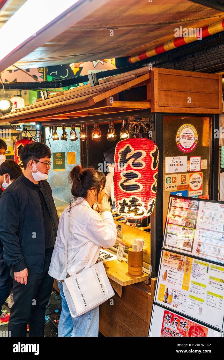 Des Japonais attendent le soir au comptoir à emporter du restaurant Takohachi servant des takoyaki et okonomiyaki, à Dotonbori, Osaka. Banque D'Images