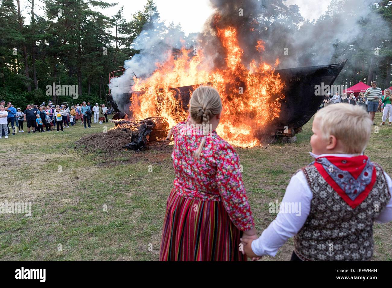 Garçon local et fille vêtus d'une robe folklorique estonienne célébrant la jaanipaeva ou la journée du milieu de l'été avec feu de joie (bateau à voile brûlant) à l'arrière, estonie Banque D'Images