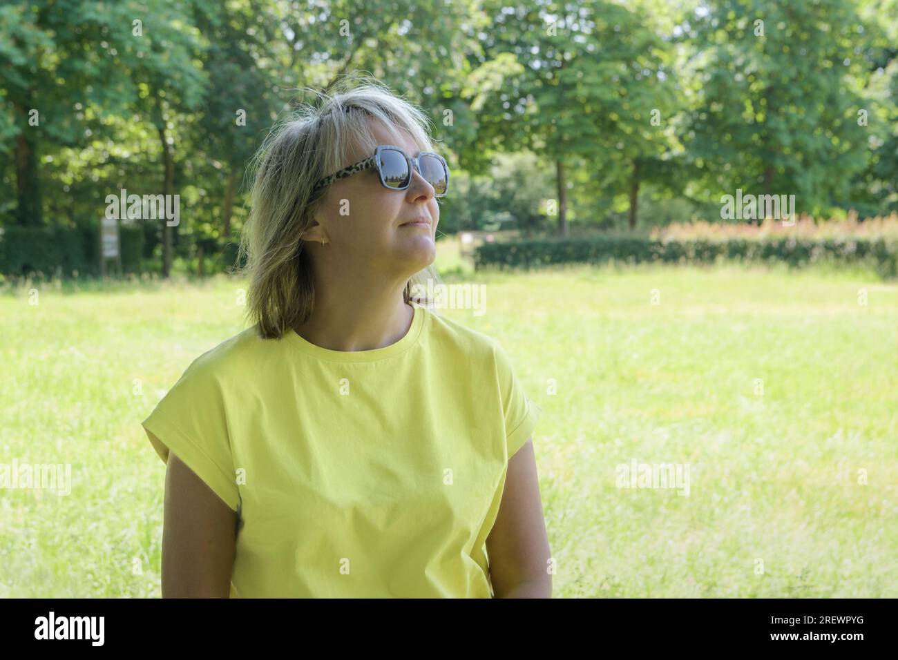Portrait d'été d'une femme blonde avec en toile de fond une pelouse herbeuse et des arbres dans le parc Banque D'Images