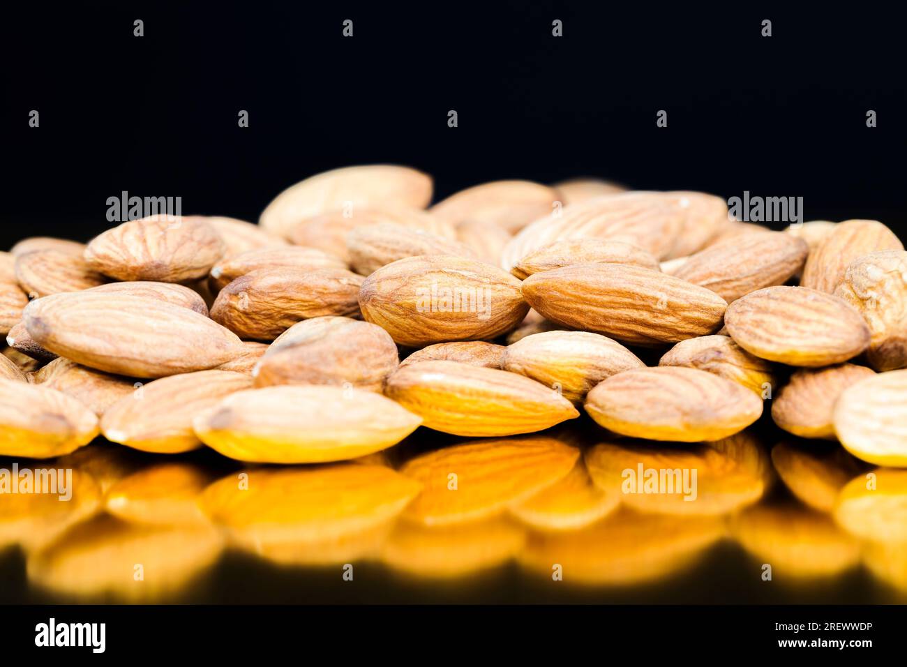 amandes fraîches crues empilées en pile sur une surface miroir noire, gros plan de produits alimentaires naturels Banque D'Images