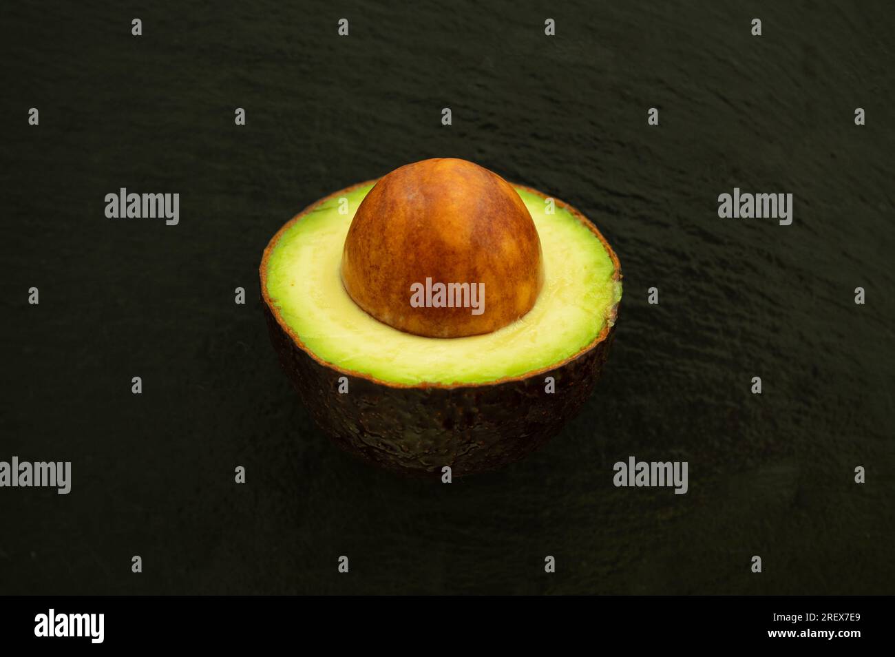 Demi avocat avec des graines dépassant sur fond noir - Superfood sain Banque D'Images