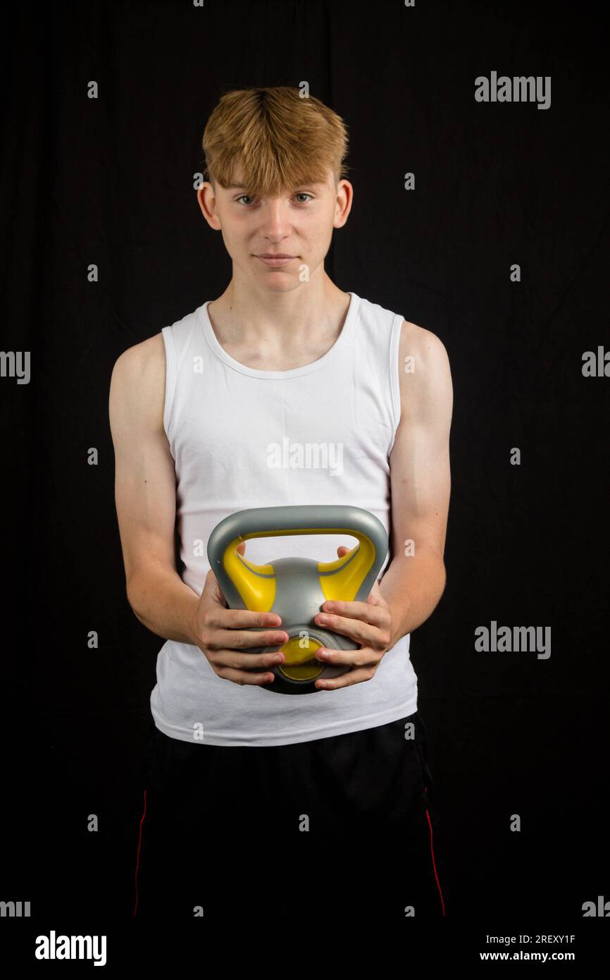 Portrait d'un adolescent caucasien de 14 ans portant un gilet sans manches tenant une kettlebell contre un garçon de fond noir Banque D'Images