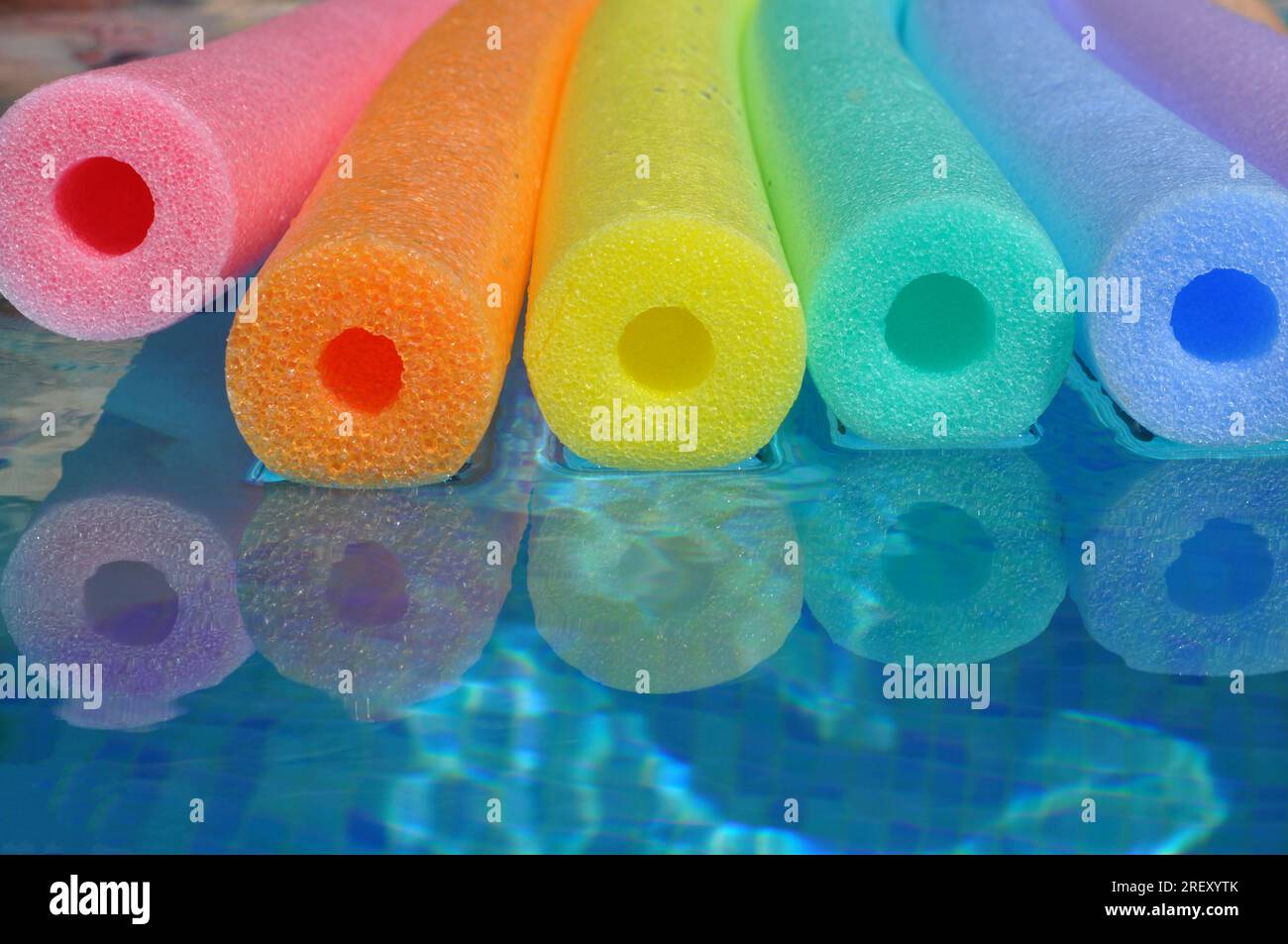 Nouilles de piscine en polyéthylène couleur arc-en-ciel flottant dans une piscine carrelée bleue, vibrations estivales Banque D'Images