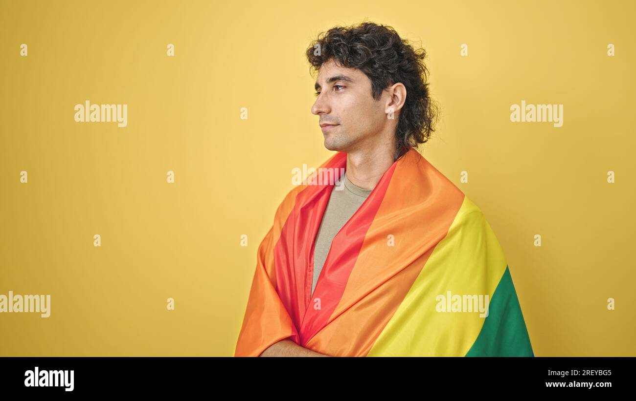 Jeune homme hispanique portant le drapeau arc-en-ciel avec une expression détendue sur fond jaune isolé Banque D'Images