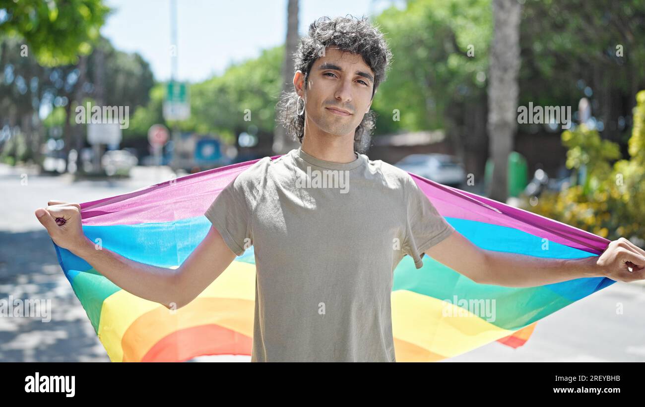 Jeune homme hispanique portant un drapeau arc-en-ciel avec expression détendue dans la rue Banque D'Images
