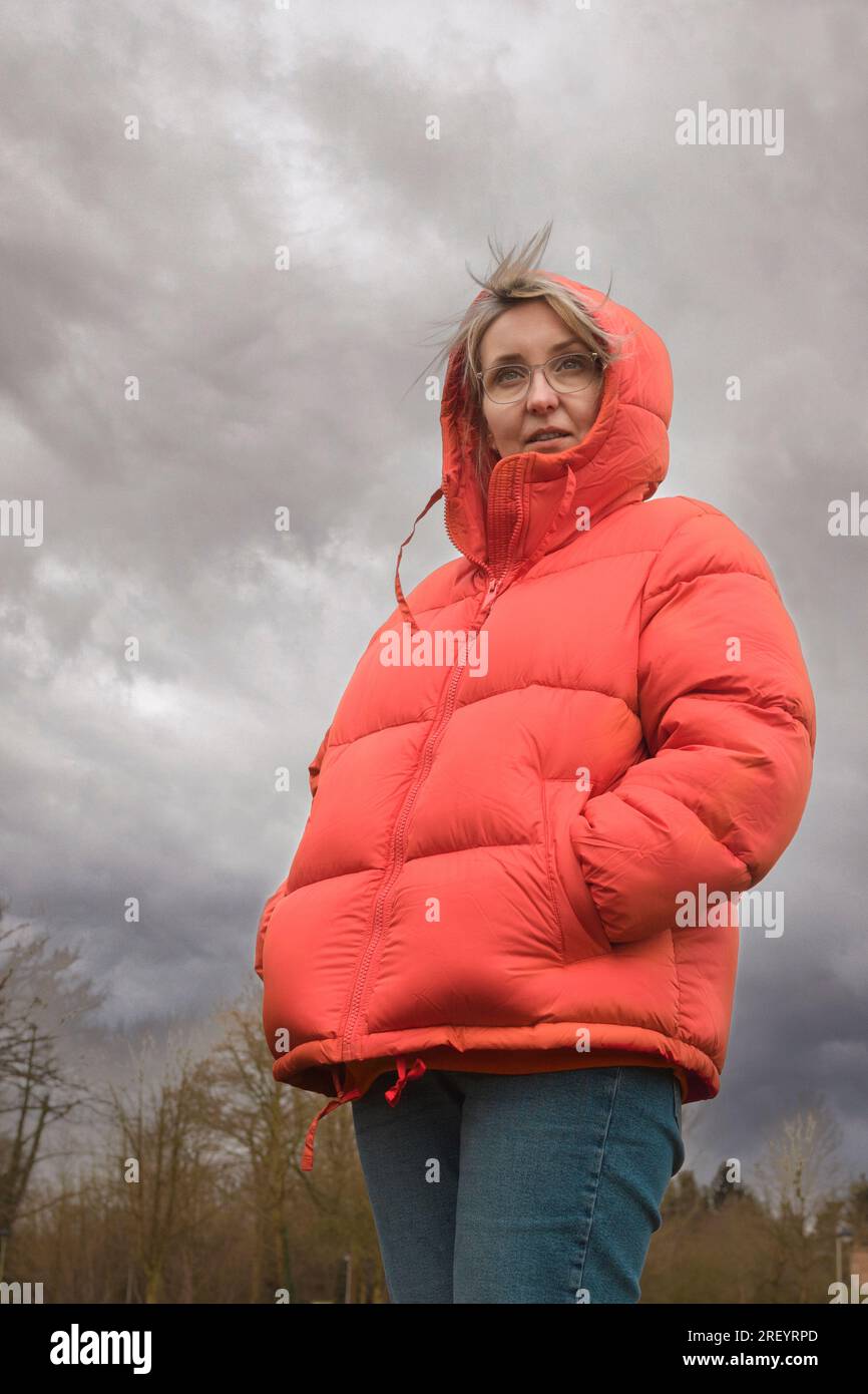 Vêtements pour femmes par mauvais temps. Femme dans une veste rouge. Portrait contre un ciel nuageux. Banque D'Images