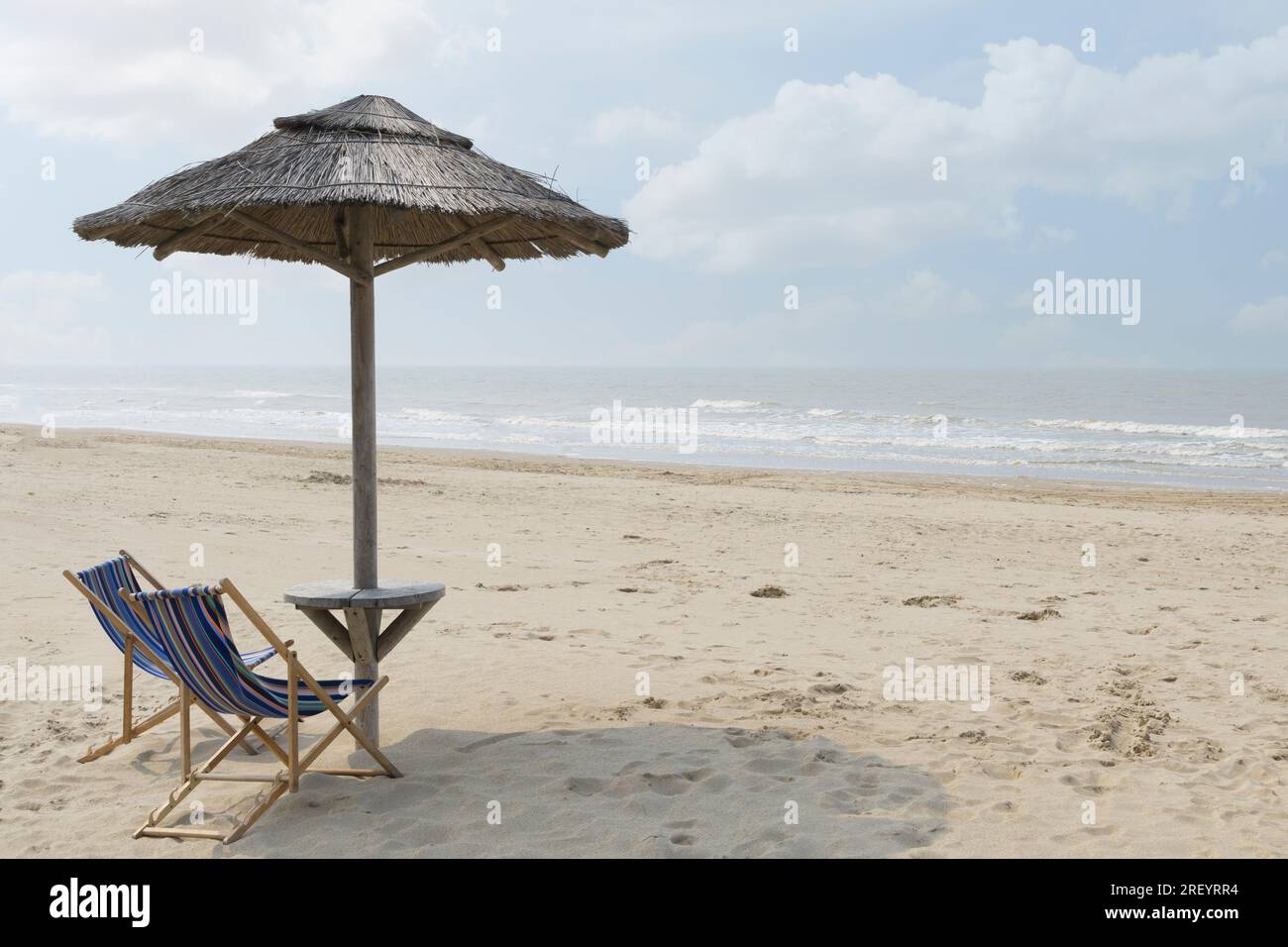 Plage déserte quelque part sur la mer. Deux chaises de plage, un parasol en paille. Personne Banque D'Images