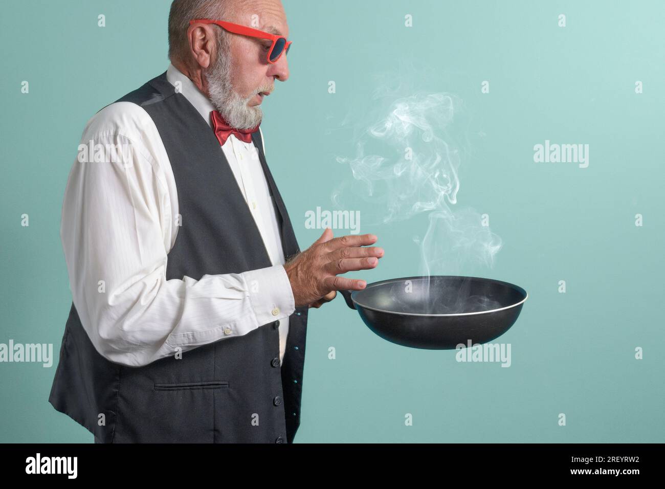 Commande de cuisine. Agitation festive. Un homme avec une poêle à frire fumante à la main. Sur fond vert clair Banque D'Images