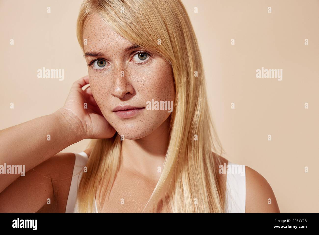 Jeune belle femme blonde avec des taches de rousseur regardant la caméra et ajustant ses cheveux Banque D'Images