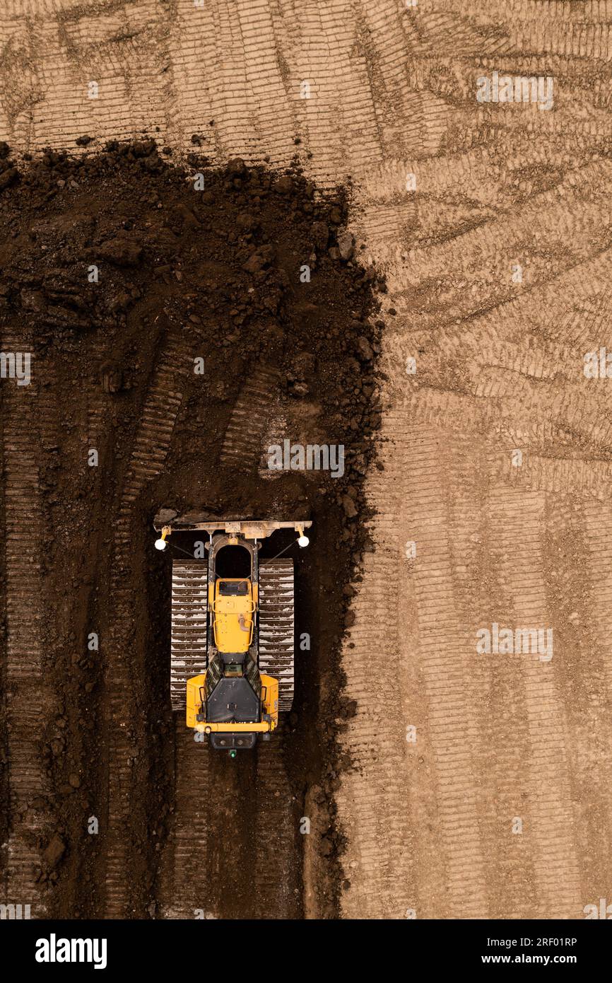 Vue aérienne directement au-dessus d'un bulldozer ou d'une machine de terrassement avec des chenilles poussant la terre et le sol dans l'industrie de la construction sur un site de friches industrielles wi Banque D'Images