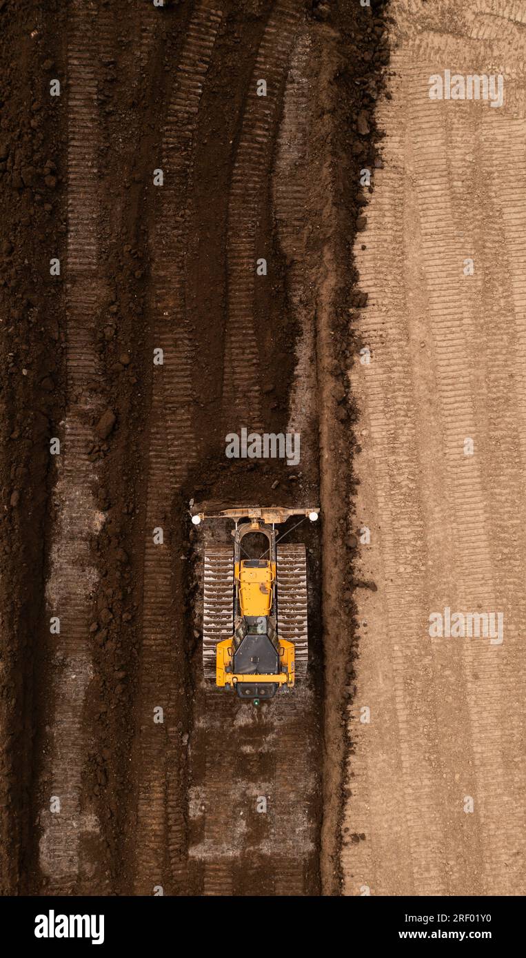 Vue aérienne directement au-dessus d'un bulldozer ou d'une machine de terrassement avec des chenilles poussant la terre et le sol dans l'industrie de la construction sur un site de friches industrielles wi Banque D'Images