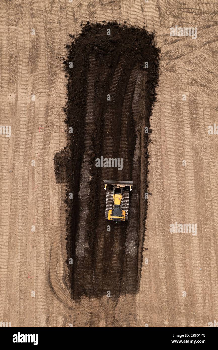 Vue aérienne directement au-dessus d'un bulldozer ou d'une machine de terrassement avec des chenilles poussant la terre et le sol dans l'industrie de la construction sur un site de friches industrielles wi Banque D'Images