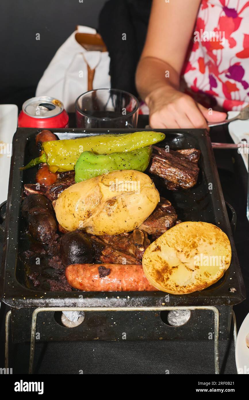 Gros plan de viande avec des légumes assortis sur le gril à charbon et une personne méconnaissable derrière. Alimentation saine et concept de cuisine. Banque D'Images