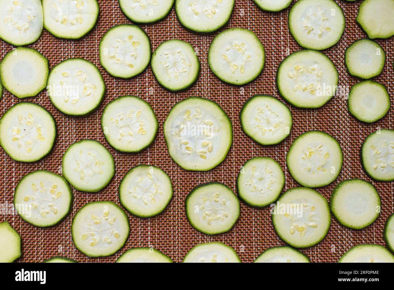 Une photo de pose plate de petites tranches de courgettes disposées sur un tapis séchant au soleil. Banque D'Images