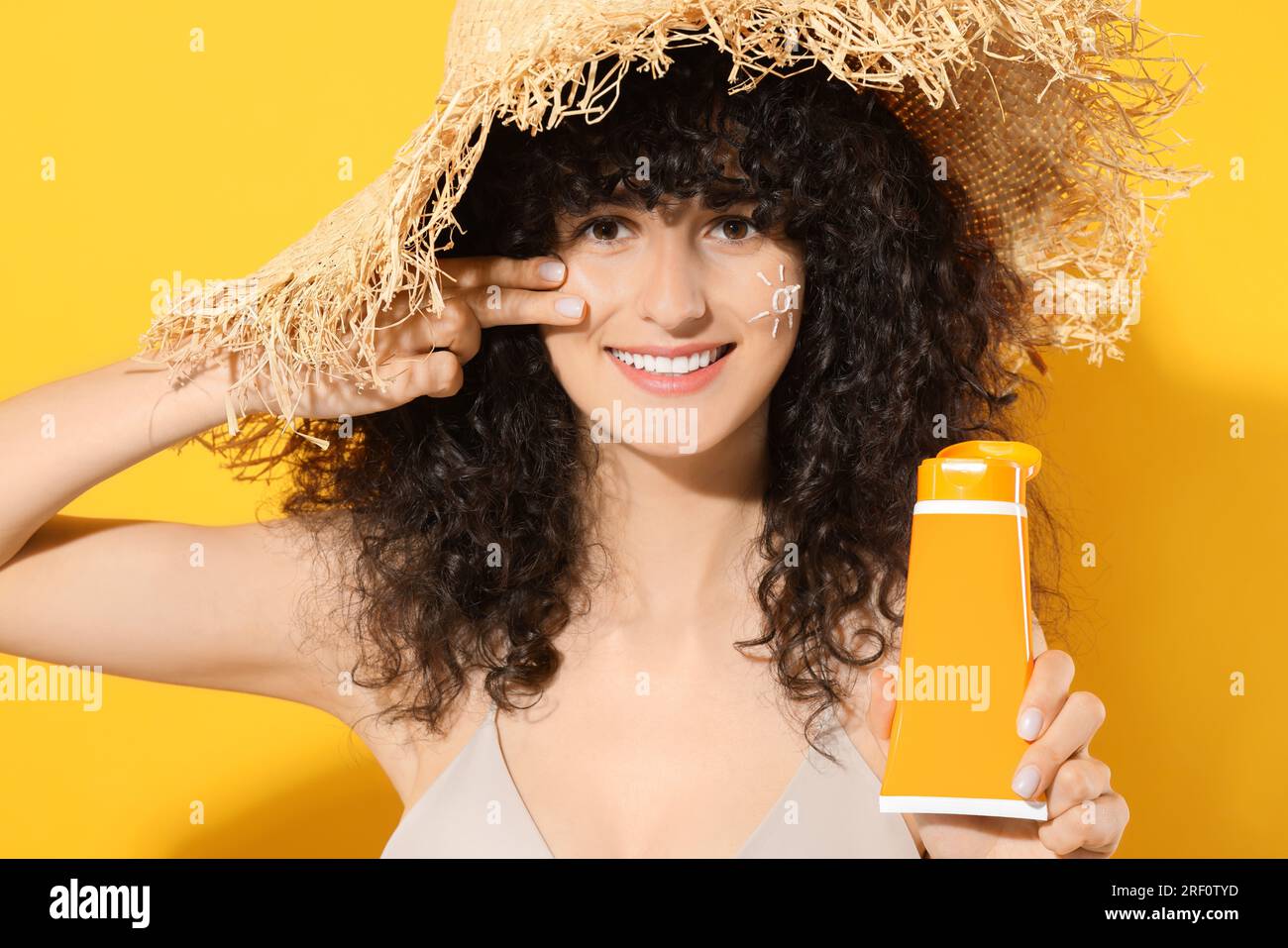 Belle jeune femme dans le chapeau de paille tenant le tube de crème solaire sur fond orange Banque D'Images