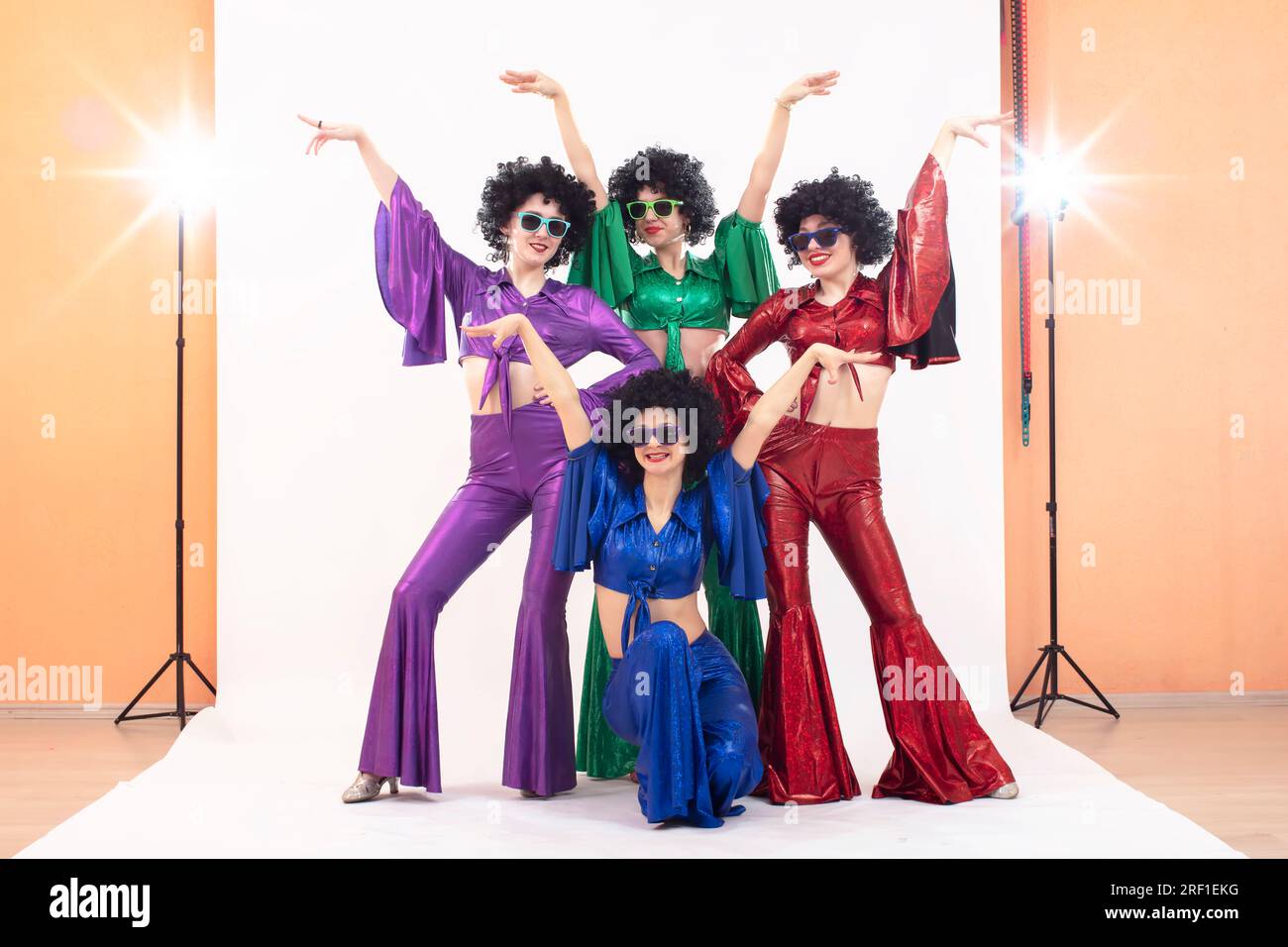 Un groupe de filles en costumes évasés colorés et perruques afro posent dans un studio photo. Style disco des années 80 ou 70. Banque D'Images
