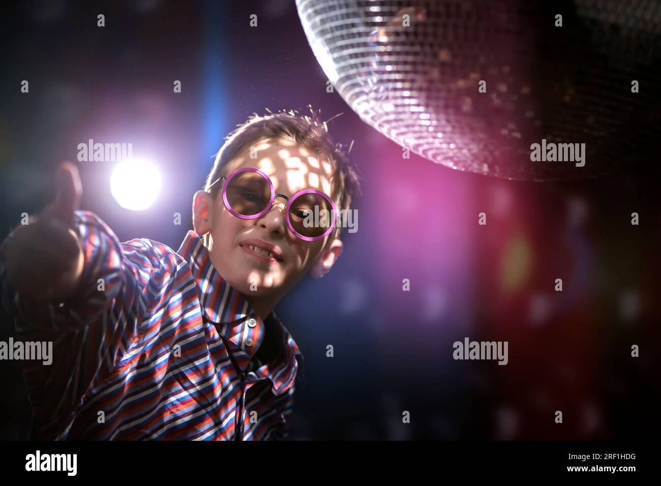 Un jeune garçon dans des lunettes élégantes montre un signe de classe sur  fond de rayons lumineux d'une boule disco. Discothèque pour enfants, fête  Photo Stock - Alamy