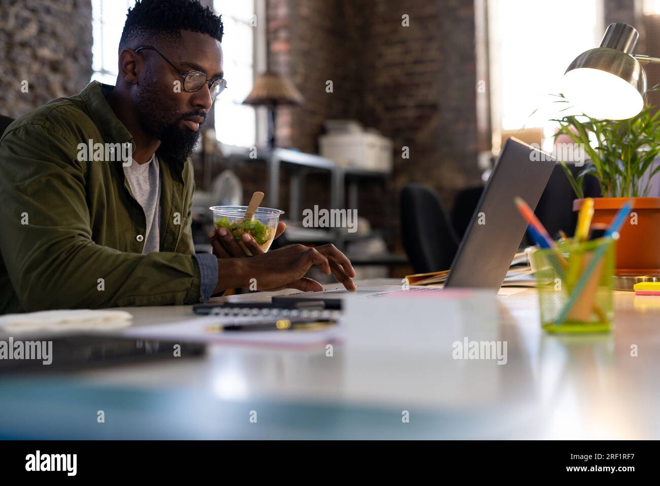 Homme d'affaires occasionnel afro-américain utilisant un ordinateur portable et mangeant de la salade à emporter assis au bureau dans le bureau Banque D'Images
