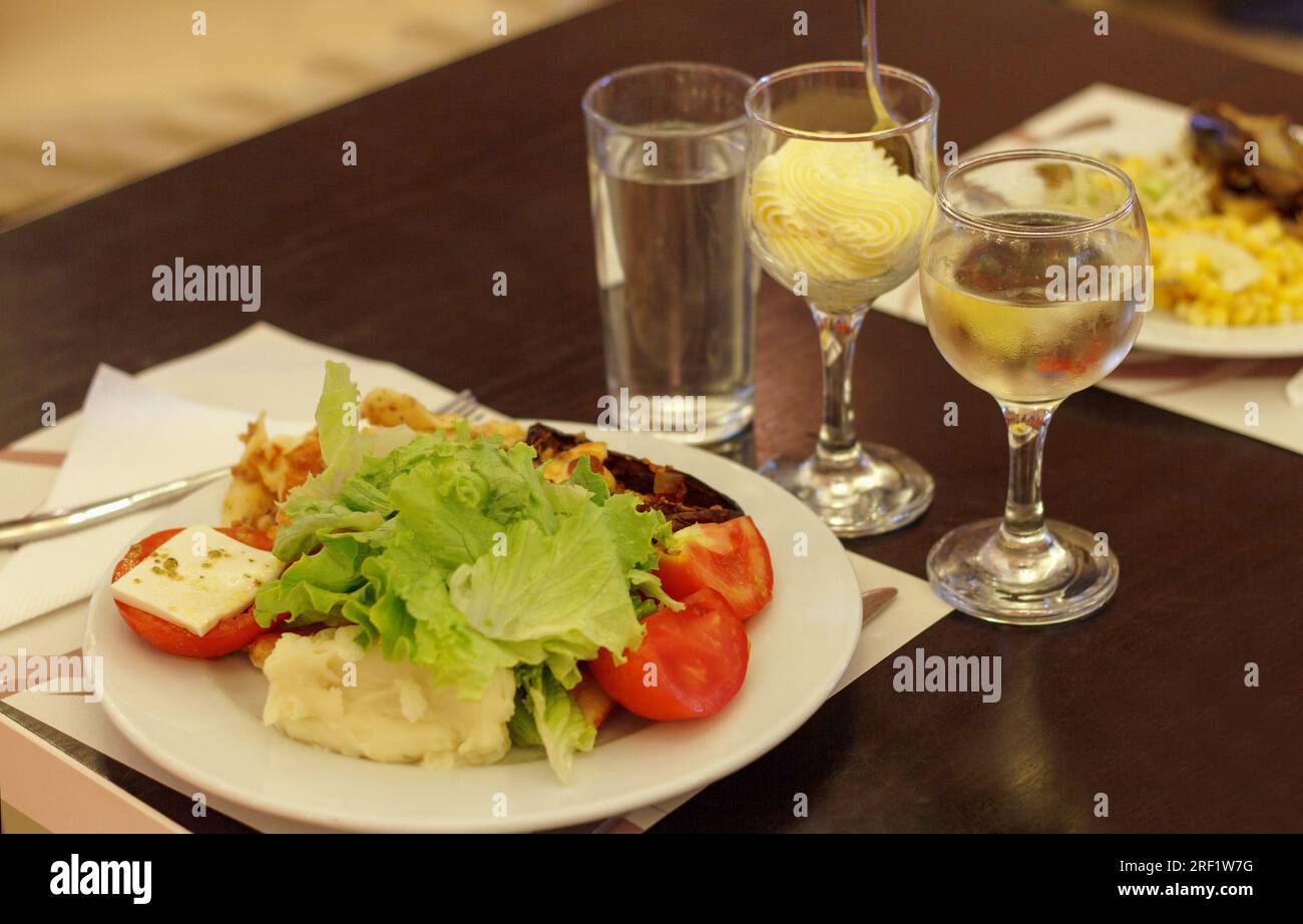 Déjeuner léger dans la salle à manger. Une assiette de salade, tomates, fromage et boissons avec un dessert sucré Banque D'Images