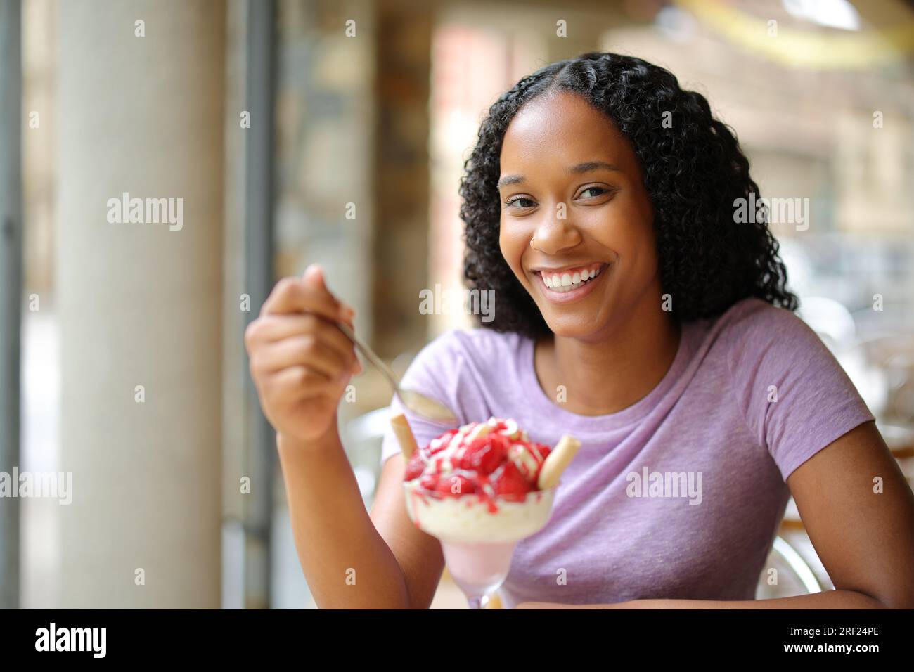 Heureuse femme noire mangeant le dessert dans une terrasse de restaurant regardant la caméra Banque D'Images