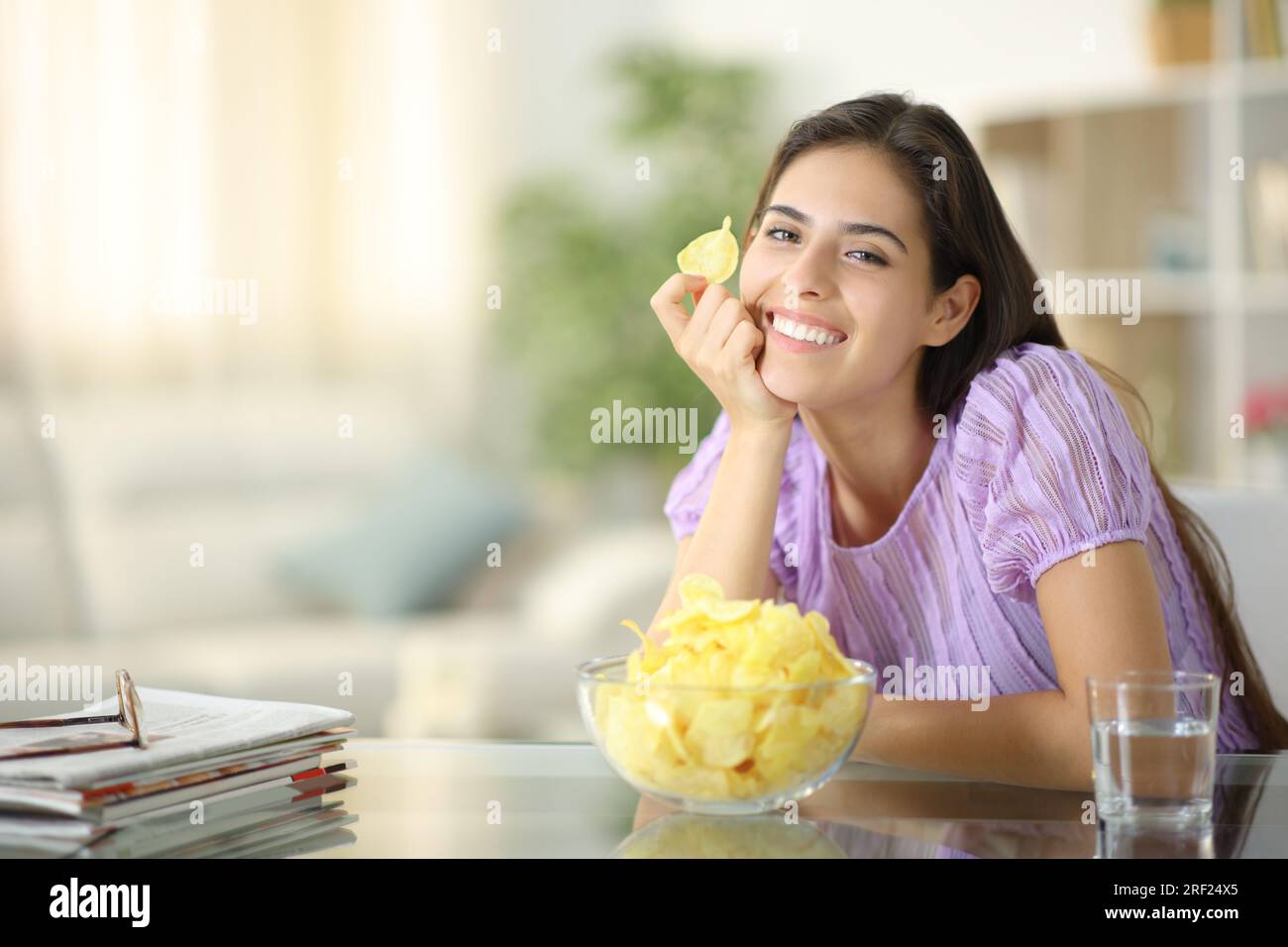 Femme heureuse posant avec chip potatos vous regardant à la maison Banque D'Images