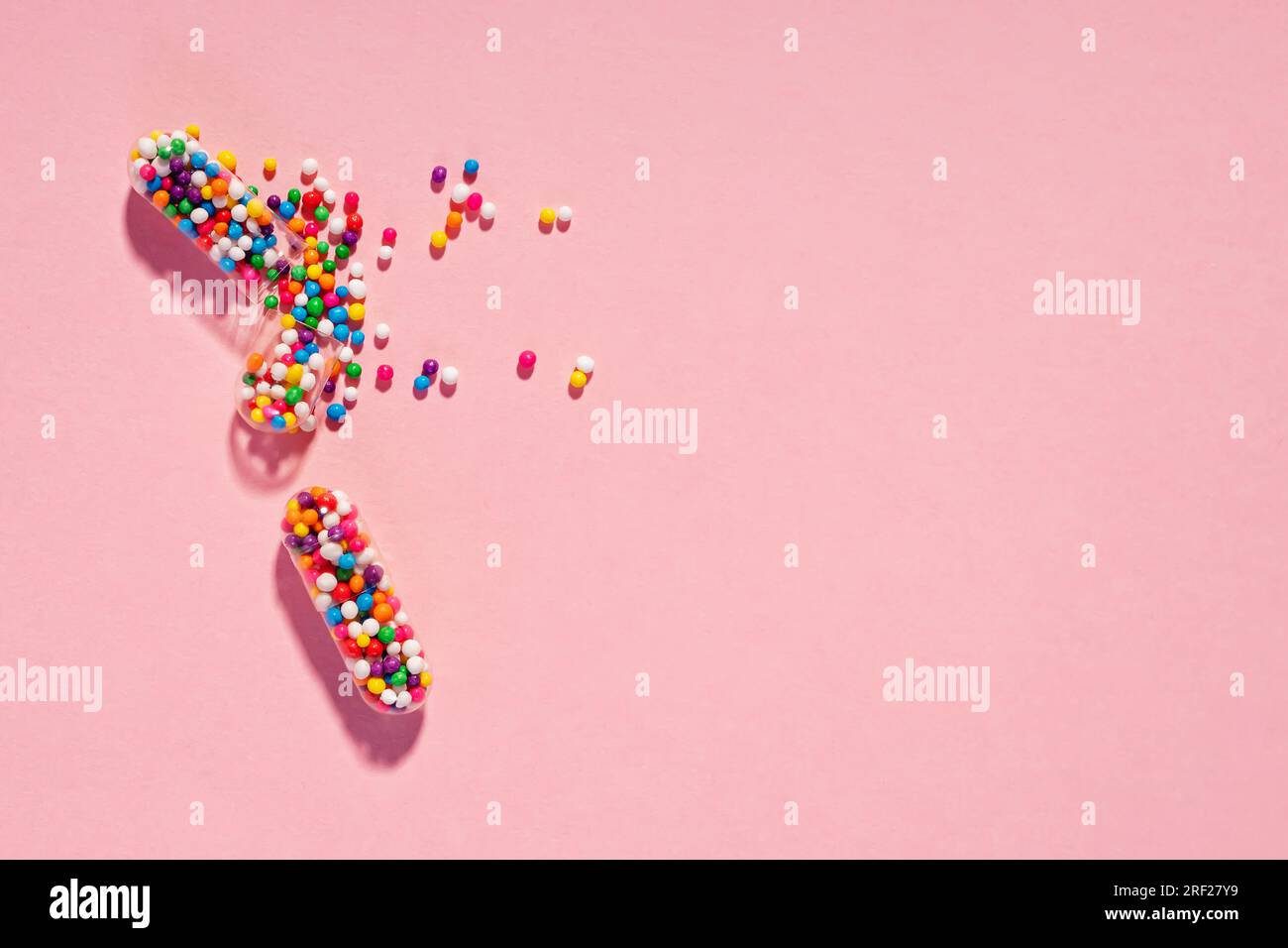 Capsules de pilule médicale remplies de saupoudrages de sucre colorés sur fond rose. Concept de santé créatif Banque D'Images