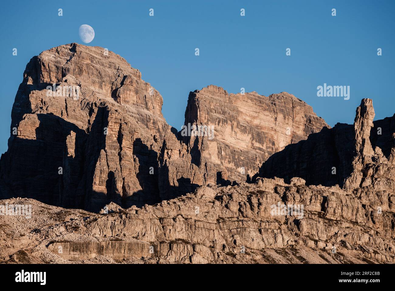 Sommets des montagnes rocheuses à l'heure de lever de la lune sur le ciel bleu. Banque D'Images