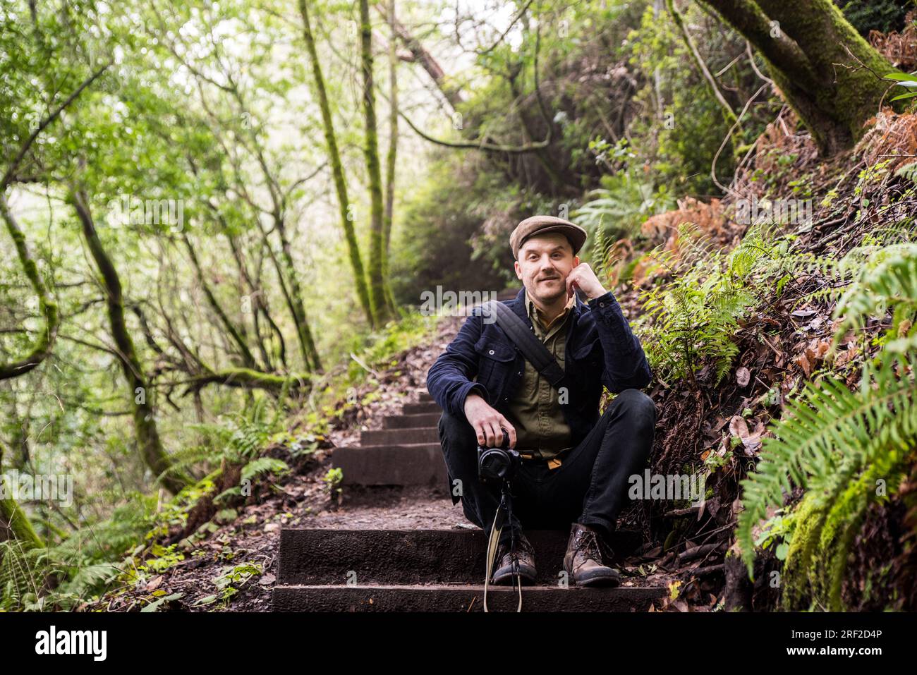 Homme souriant à la caméra et assis sur des marches en bois dans la forêt Banque D'Images