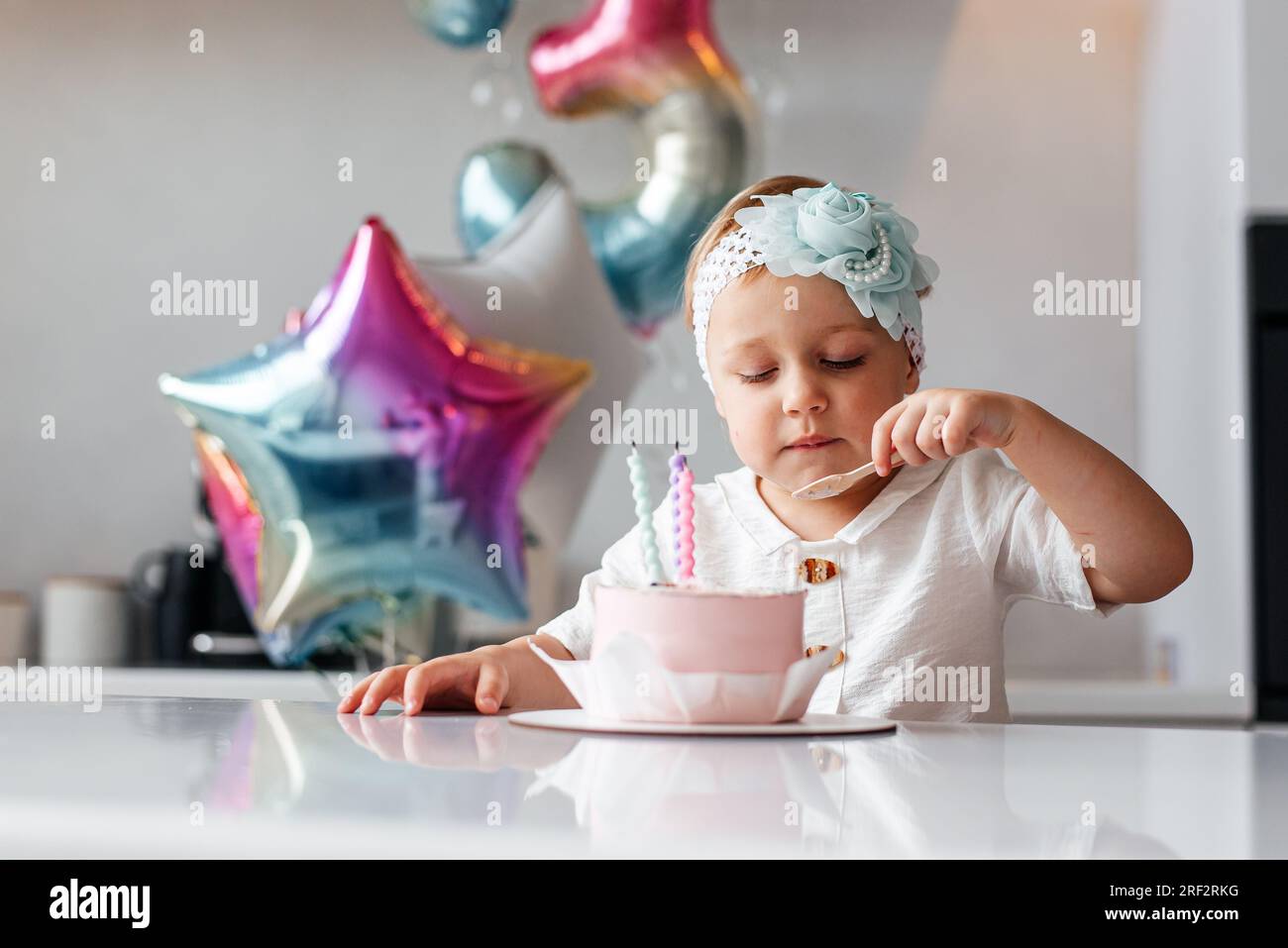Adorable enfant de trois ans célébrant son anniversaire et soufflant des bougies sur un gâteau cuit maison, à l'intérieur Banque D'Images