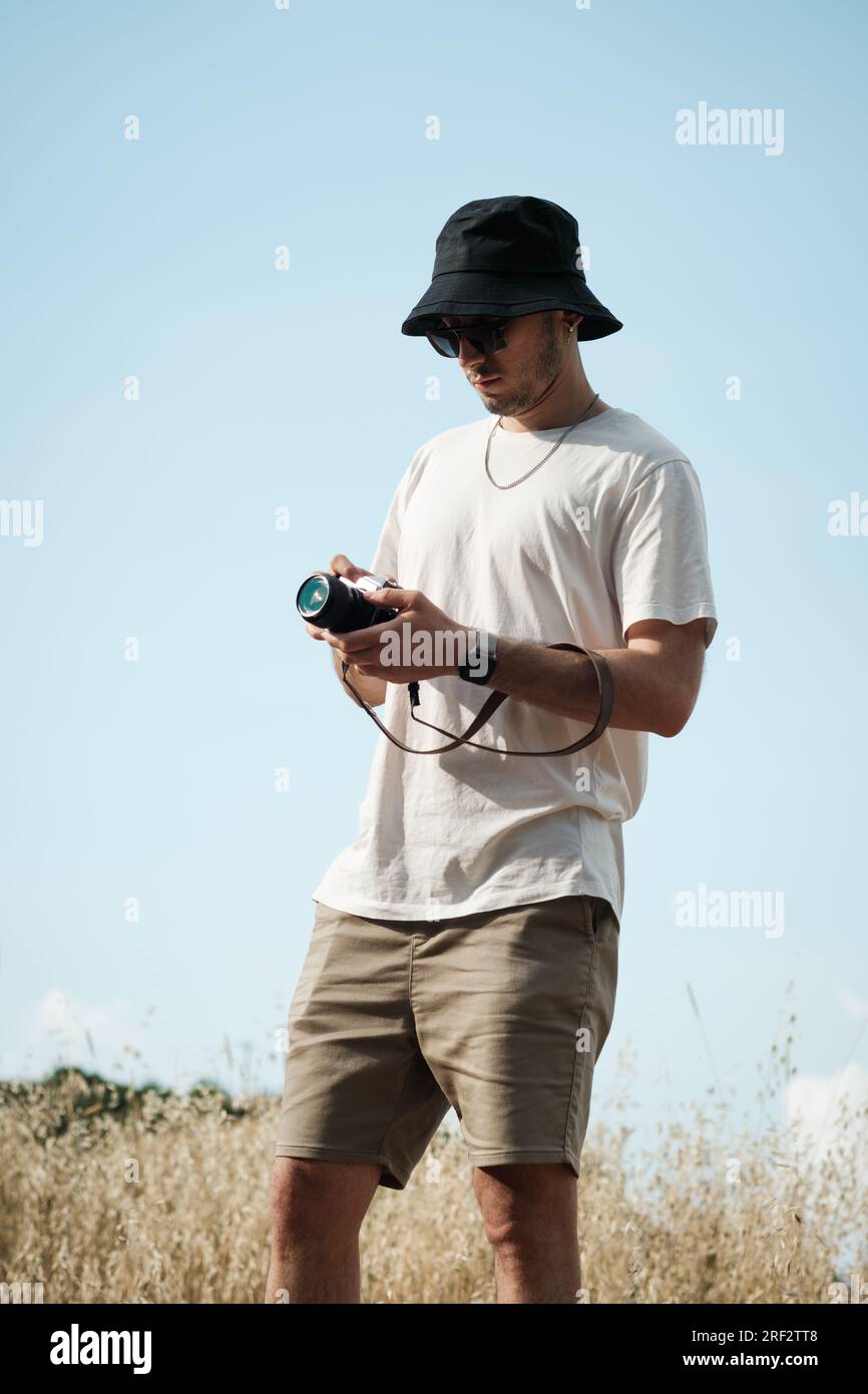 Portrait d'un homme d'une vingtaine d'années, habillé de façon décontractée d'un t-shirt blanc, d'un short beige, de lunettes de soleil et d'une casquette de marin noire, avec un camouflage classique Banque D'Images