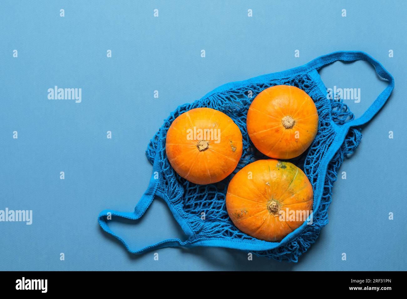 Citrouilles jaunes dans un sac à ficelle en coton sur fond bleu. Vue de dessus, pose à plat, espace de copie. Thanksgiving et halloween concept. Banque D'Images