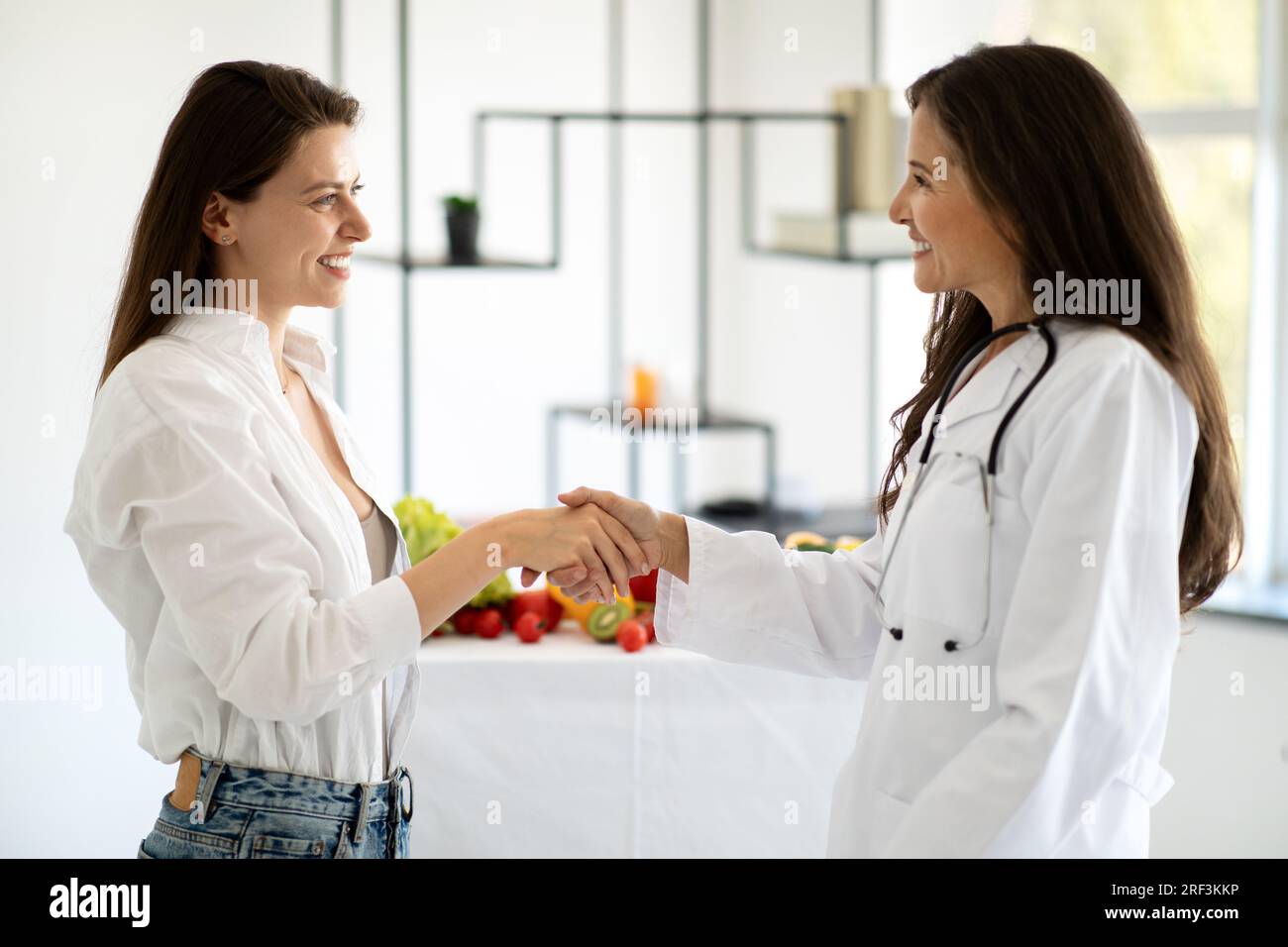 Joyeuse dame européenne d'âge moyen médecin nutritionniste en manteau blanc conseille le patient de femme millénaire, serrant la main Banque D'Images