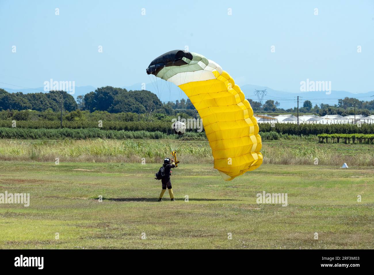 Vue imprenable sur un parachutiste avec un parachute jaune atterrissant sur une pelouse verte pendant une journée ensoleillée. Banque D'Images