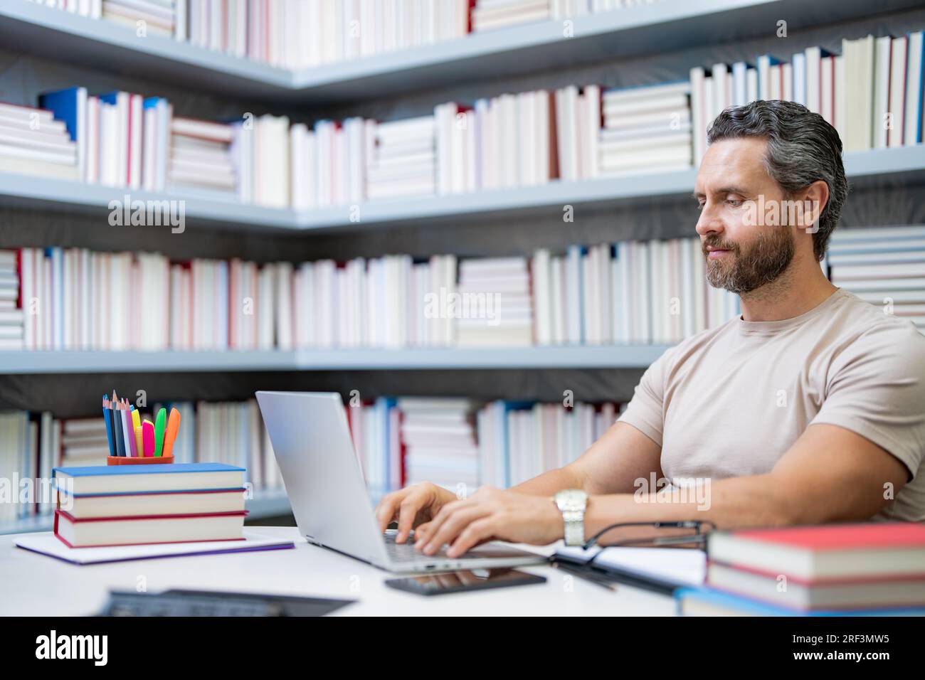 Professeur avec ordinateur portable dans la salle de classe de la bibliothèque. Beau travail de professeur sur ordinateur portable dans la bibliothèque universitaire. Journée des enseignants. Enseignant utilisant un ordinateur portable donnant des cours Banque D'Images