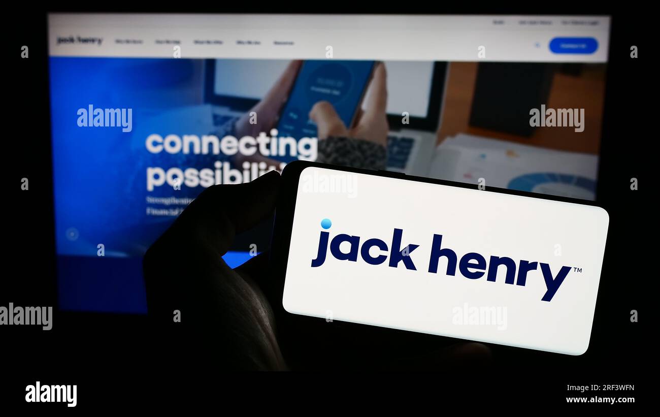Personne détenant un smartphone avec le logo de la société financière américaine Jack Henry Associates Inc. Sur l'écran devant le site Web. Concentrez-vous sur l'affichage du téléphone. Banque D'Images