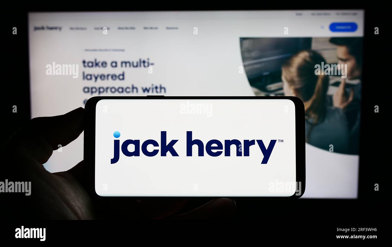 Personne détenant un téléphone portable avec le logo de la société financière américaine Jack Henry Associates Inc. Sur l'écran devant la page Web. Concentrez-vous sur l'affichage du téléphone. Banque D'Images