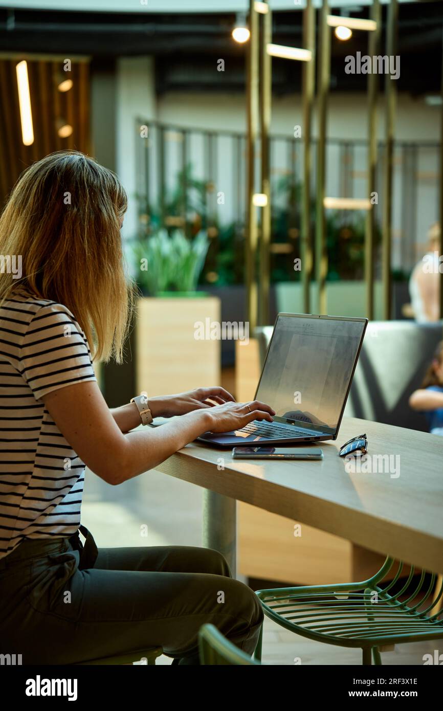 Femme utilisant un ordinateur portable dans le coworking avec des plantes vertes. Femme freelancer tapant sur le clavier d'ordinateur portable. Travail en ligne dans le café Banque D'Images