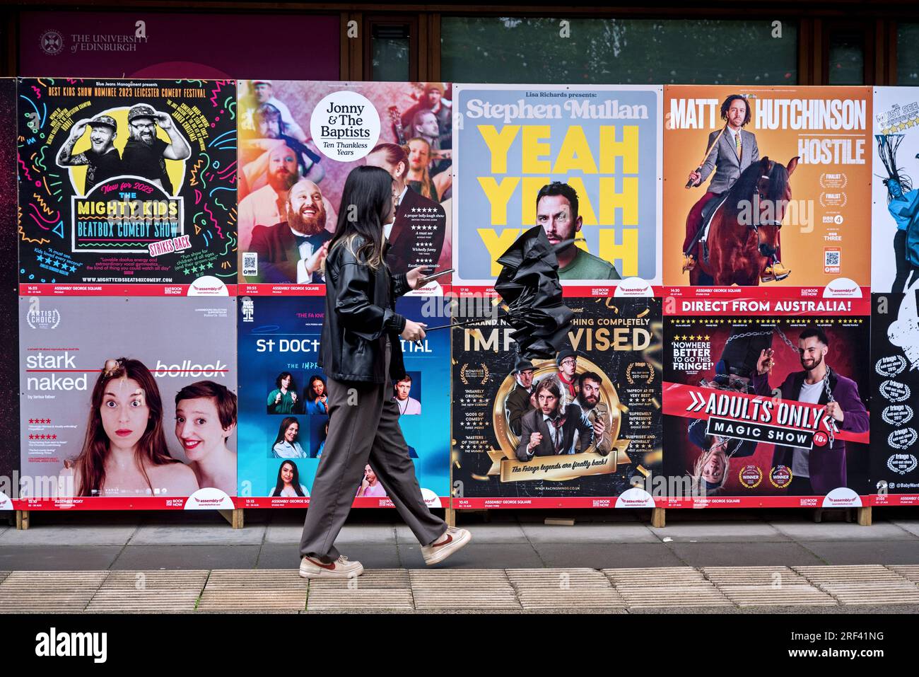 Jeune femme marchant par des affiches publicitaires pour des spectacles au Festival Fringe d'Édimbourg à George Square, Édimbourg, Écosse, Royaume-Uni. Banque D'Images