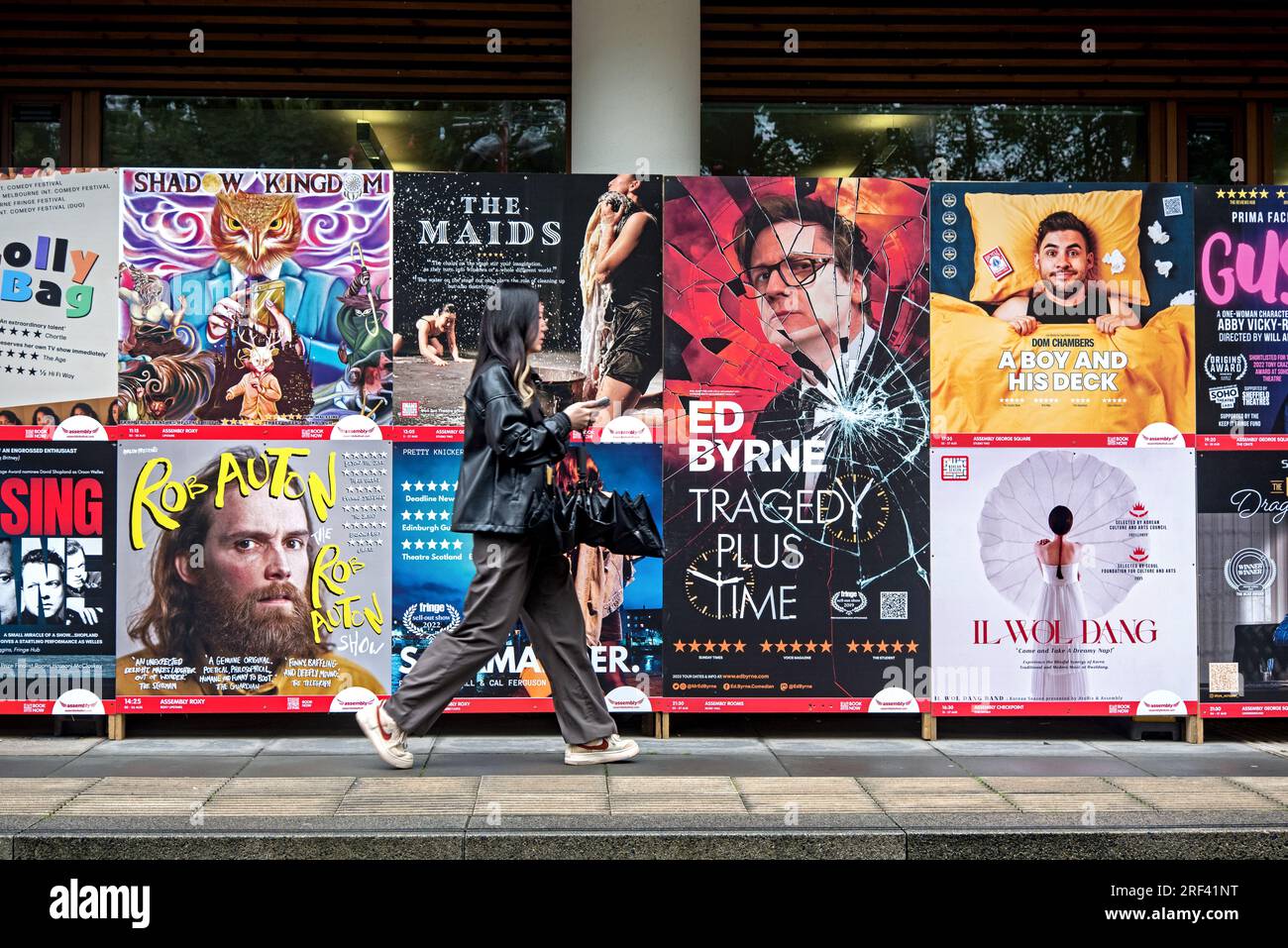 Jeune femme marchant par des affiches publicitaires pour des spectacles au Festival Fringe d'Édimbourg à George Square, Édimbourg, Écosse, Royaume-Uni. Banque D'Images