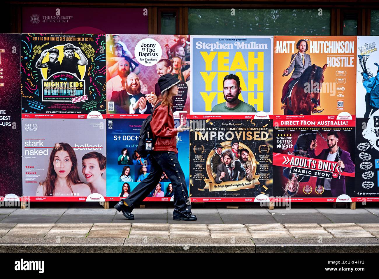 Jeune femme marchant par des affiches publicitaires pour des spectacles au Festival Fringe d'Édimbourg à George Square, Édimbourg, Écosse, Royaume-Uni. Banque D'Images